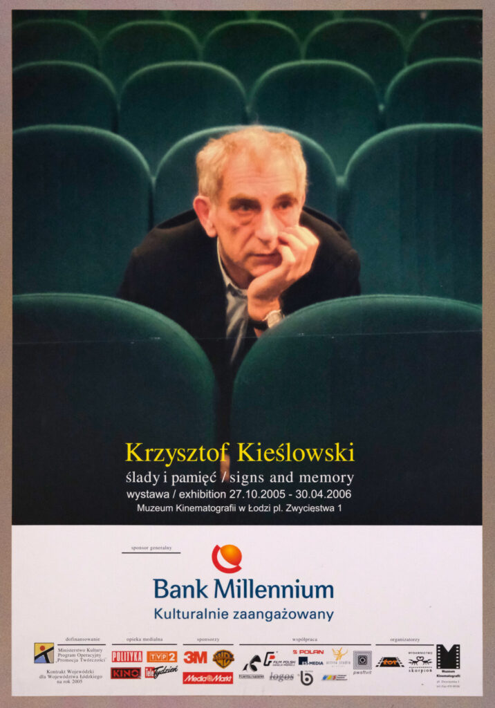 Polski plakat do wystawy „Ślady i pamięć". Krzysztof Kieślowski siedzi samotnie wśród zielonych foteli kinowych.