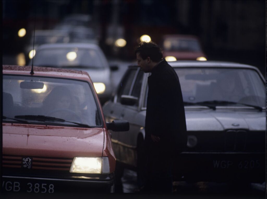 Karol (Zbigniew Zamachowski) stops a car with "Blondynka" (Grażyna Szapołowska) driving down the street.