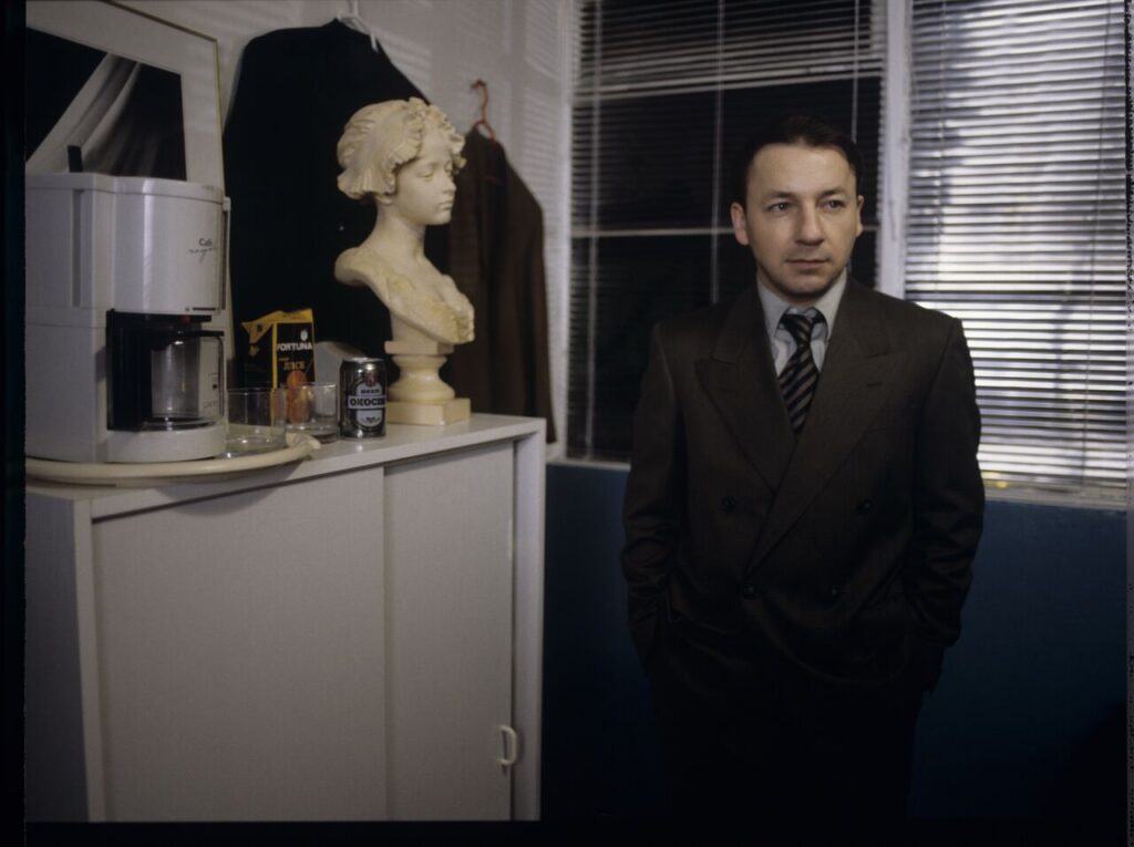 Karol (Zbigniew Zamachowski) as a businessman in his office with a plaster bust of a woman.
