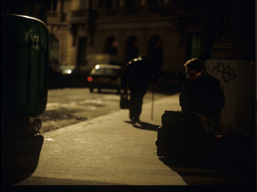Karol (Zbigniew Zamachowski) sits on the sidewalk. Next to him, a man throwing a bottle (played by the director Kieślowski).