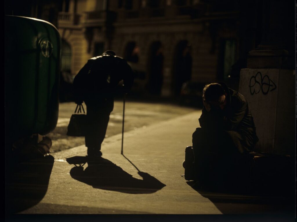 Karol (Zbigniew Zamachowski) sits on the sidewalk. Next to him, a man throwing a bottle (played by the director Kieślowski).