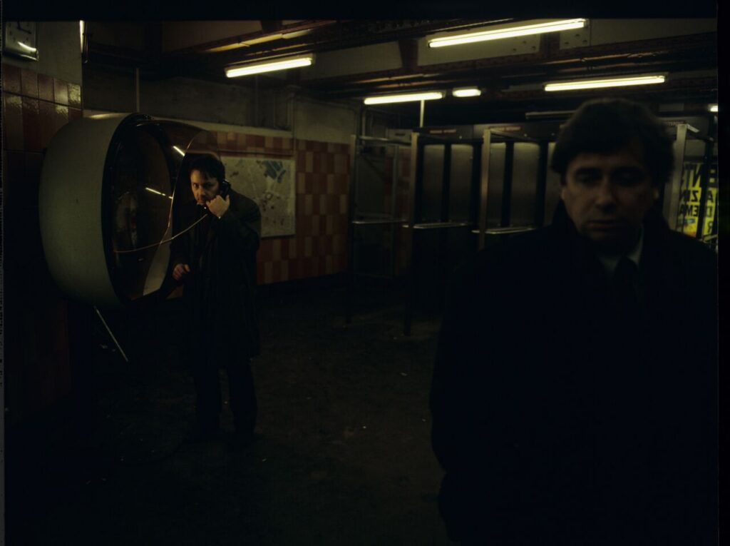 Mikołaj (Janusz Gajos) by the Paris metro. In the background Karol (Zbigniew Zamachowski) calls his wife Dominique.