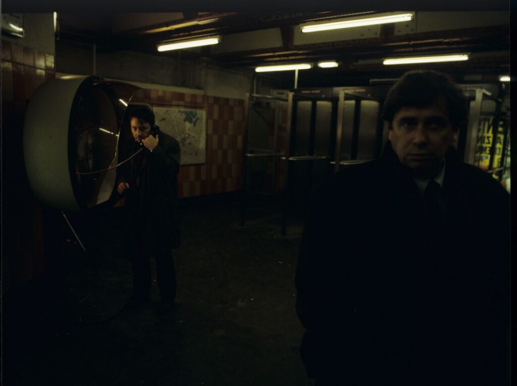 Mikołaj (Janusz Gajos) by the Paris metro. In the background Karol (Zbigniew Zamachowski) calls his wife Dominique.