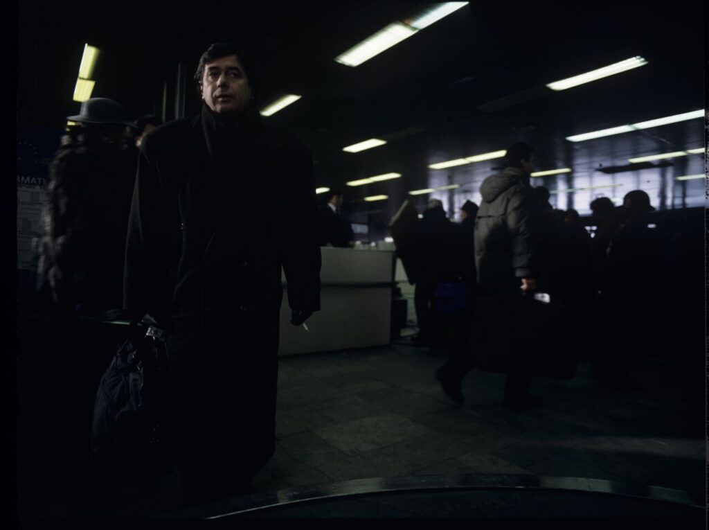 Mikołaj (Janusz Gajos) is waiting for his luggage in the arrivals hall at the Warsaw airport.
