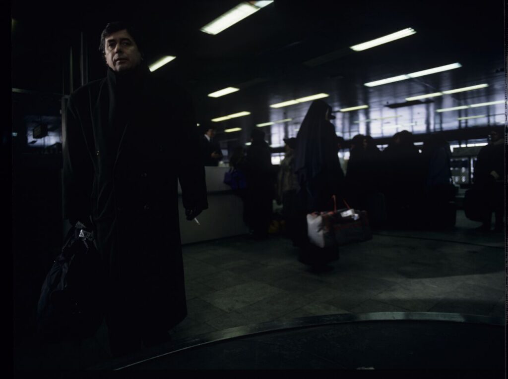 Mikołaj (Janusz Gajos) is waiting for his luggage in the arrivals hall at the Warsaw airport.