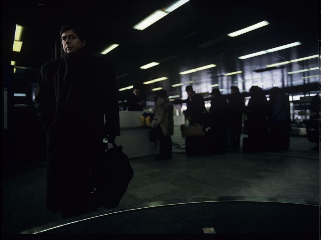 Mikołaj (Janusz Gajos) is waiting for his luggage in the arrivals hall at the Warsaw airport.