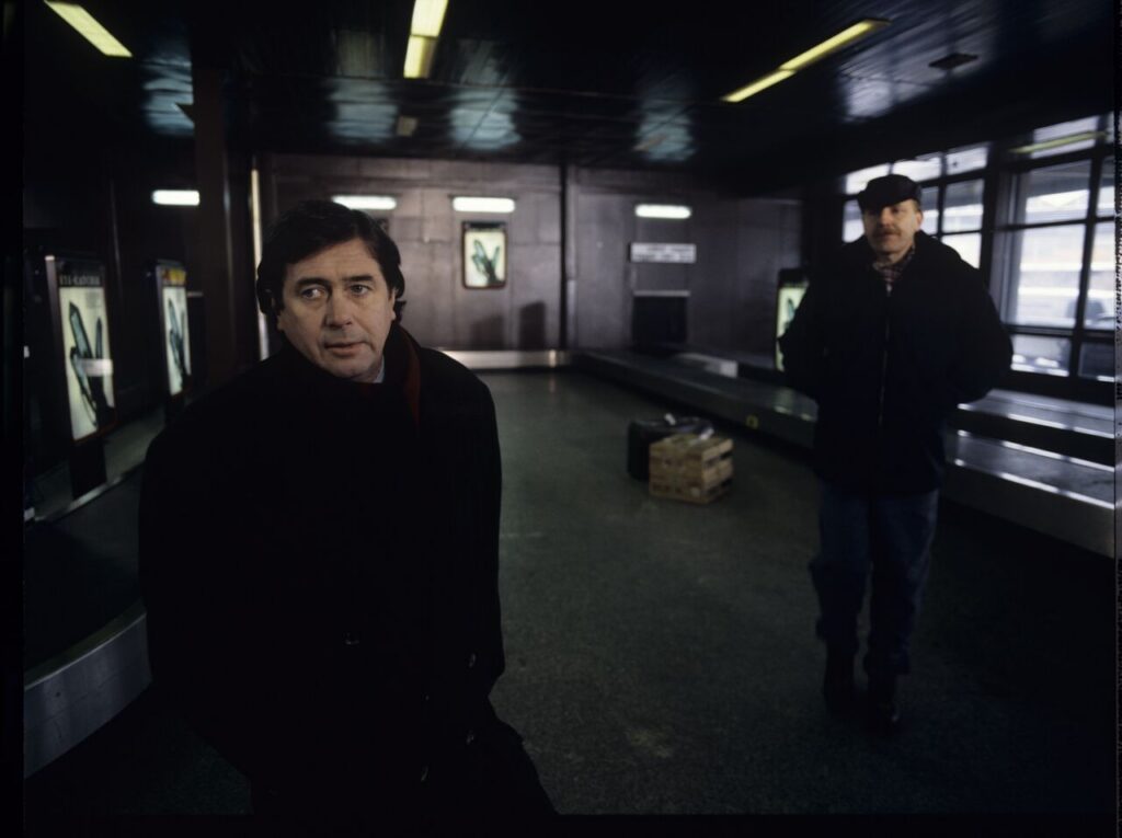 Mikołaj (Janusz Gajos) is waiting for his luggage in the arrivals hall at the Warsaw airport.