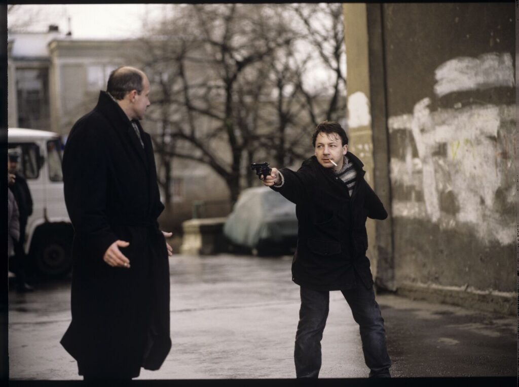 Karol (Zamachowski) distracts the attention of the man (Machalica) from the owner of the currency exchange office.