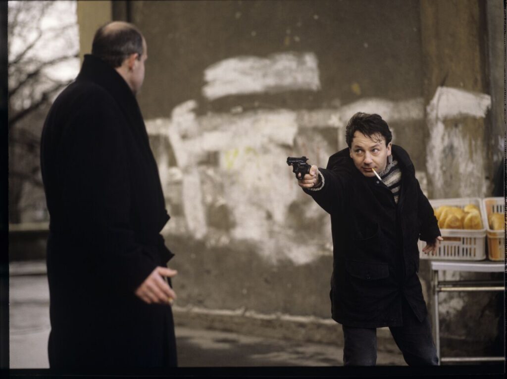 Karol (Zamachowski) distracts the attention of the man (Machalica) from the owner of the currency exchange office.