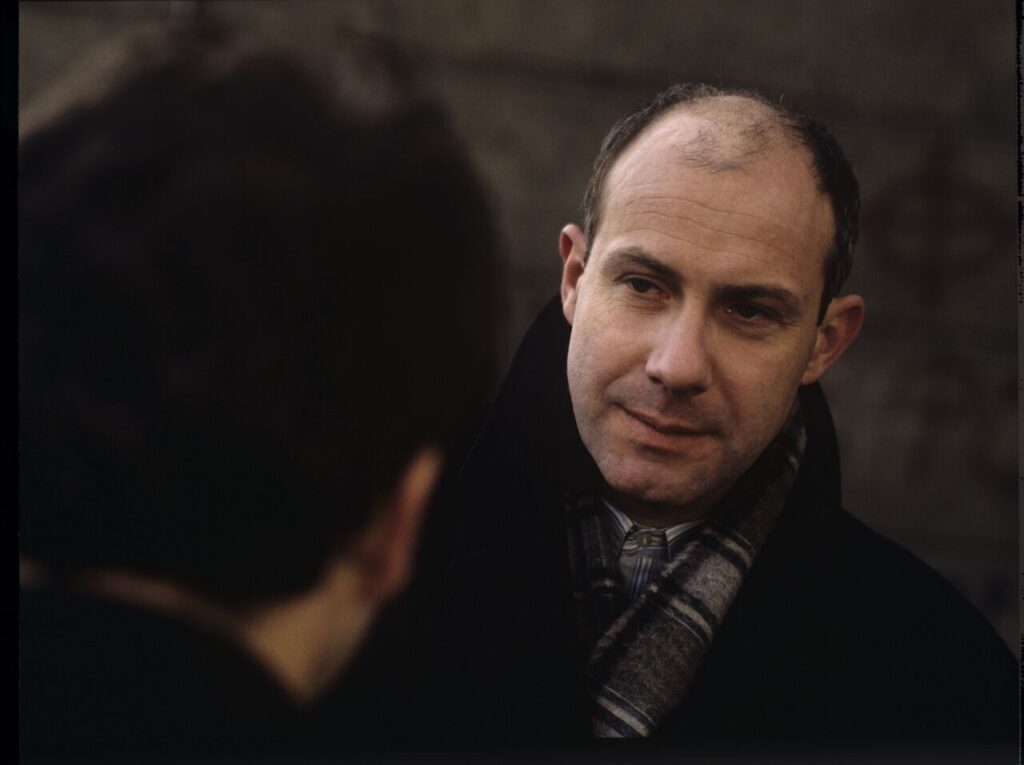 Karol (Zamachowski) distracts the attention of the man (Machalica) from the owner of the currency exchange office.