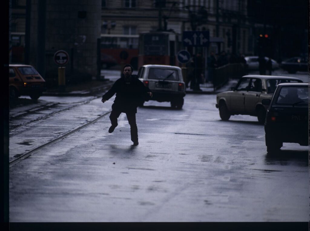 Karol (Zamachowski) tries to stop "Blondynka's" car to give her a message. The scene was not shown in the film.