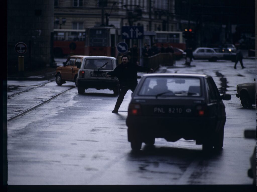 Karol (Zamachowski) tries to stop "Blondynka's" car to give her a message. The scene was not shown in the film.