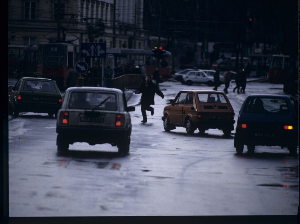 Karol (Zamachowski) tries to stop "Blondynka's" car to give her a message. The scene was not shown in the film.