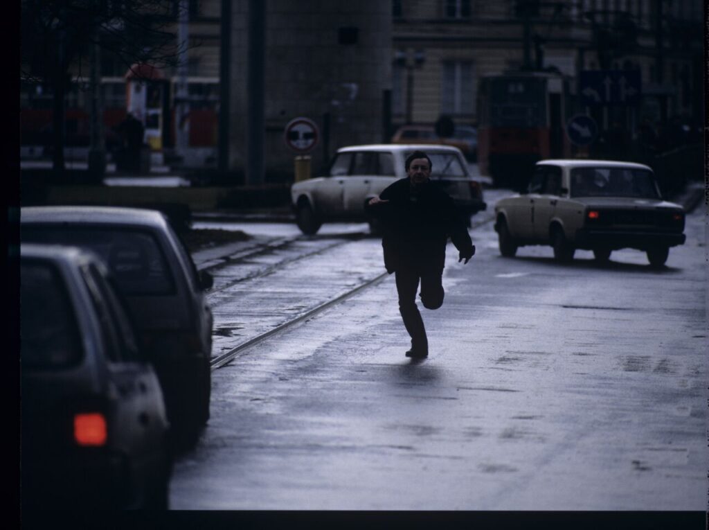 Karol (Zamachowski) tries to stop "Blondynka's" car to give her a message. The scene was not shown in the film.