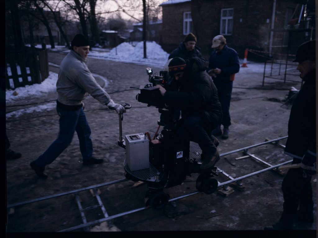 Kieślowski (director) behind the camera, surrounded by the crew, on the set in front of the house of Jurek, Karol's brother.