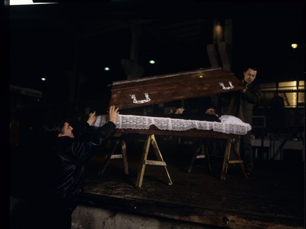 Karol (Zbigniew Zamachowski) and Mr. Bronek (Jerzy Trela) stand over the coffin of a "bought" corpse.