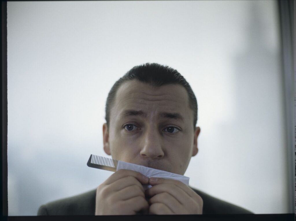 Karol (Zbigniew Zamachowski) plays a melody on a comb in his new office at the Marriott Hotel.