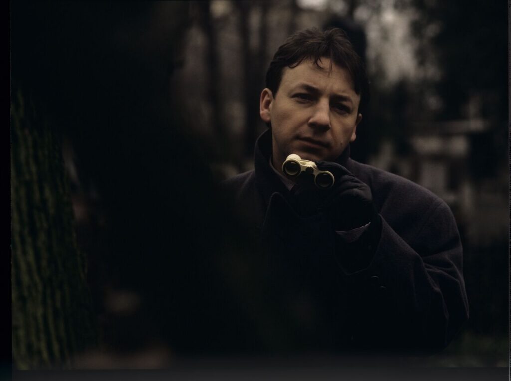 Karol (Zbigniew Zamachowski) observes his own funeral through binoculars.