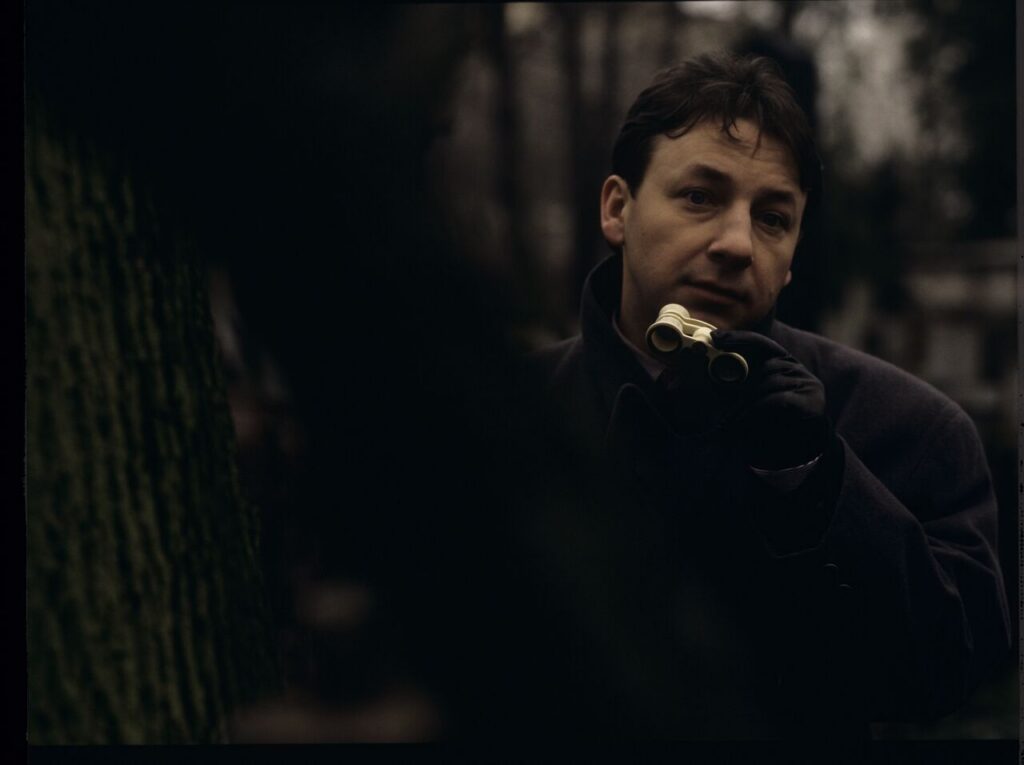 Karol (Zbigniew Zamachowski) observes his own funeral through binoculars.