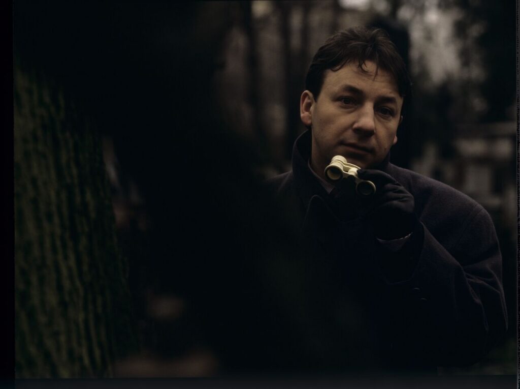 Karol (Zbigniew Zamachowski) observes his own funeral through binoculars.