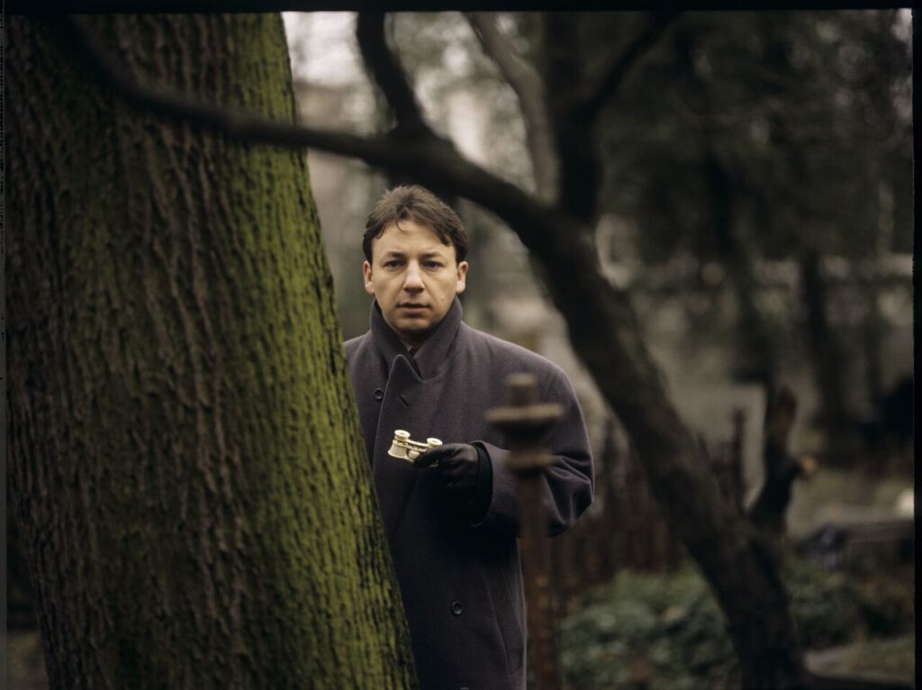 Karol (Zbigniew Zamachowski) observes his own funeral through binoculars.