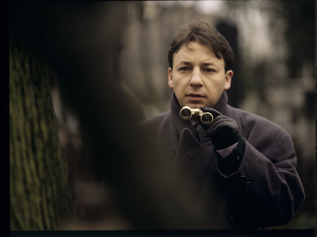 Karol (Zbigniew Zamachowski) observes his own funeral through binoculars.