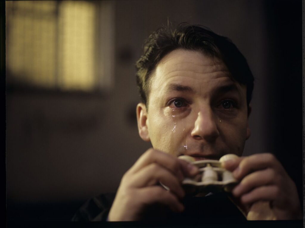 Karol (Z. Zamachowski) observes the silhouette of his ex-wife Dominique through binoculars, visible in the prison window.