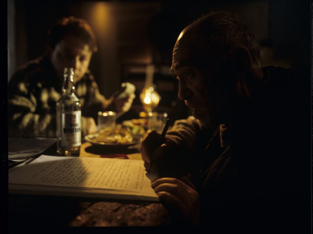 An old farmer (Jerzy Nowak) signs the land sale documents to Karol (Zbigniew Zamachowski).