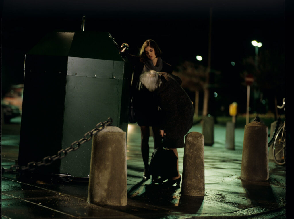 Valentina (Irène Jacob) helps an elderly woman throw a bottle into the recycling bin.
