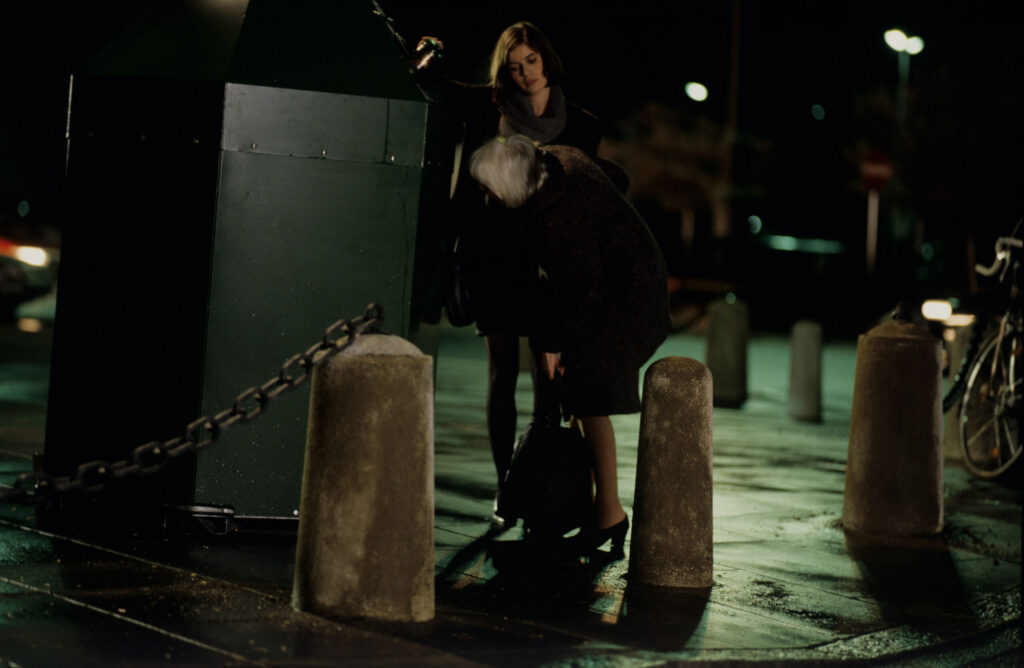 Valentina (Irène Jacob) helps an elderly woman throw a bottle into the recycling bin.