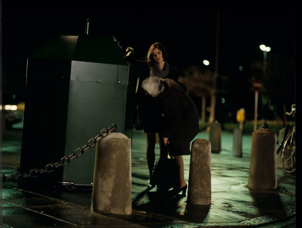 Valentina (Irène Jacob) helps an elderly woman throw a bottle into the recycling bin.