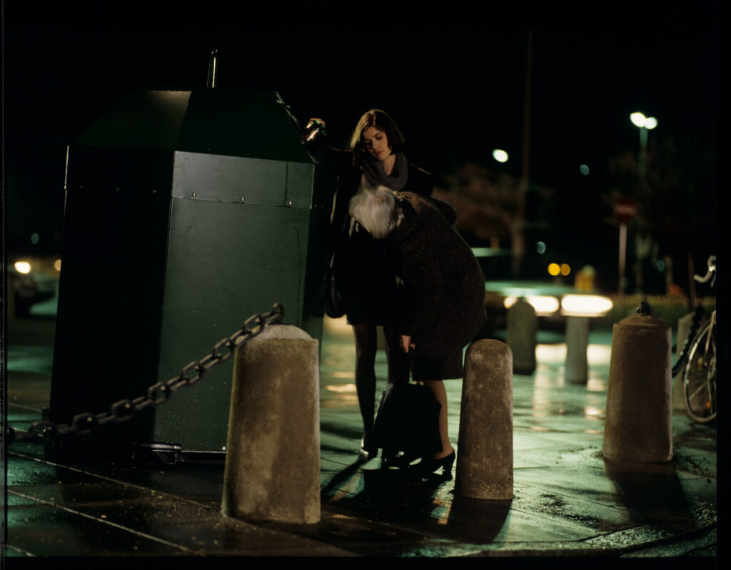 Valentina (Irène Jacob) helps an elderly woman throw a bottle into the recycling bin.