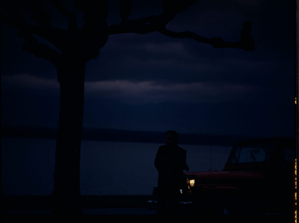 Auguste (Jean-Pierre Lorit) by the car.