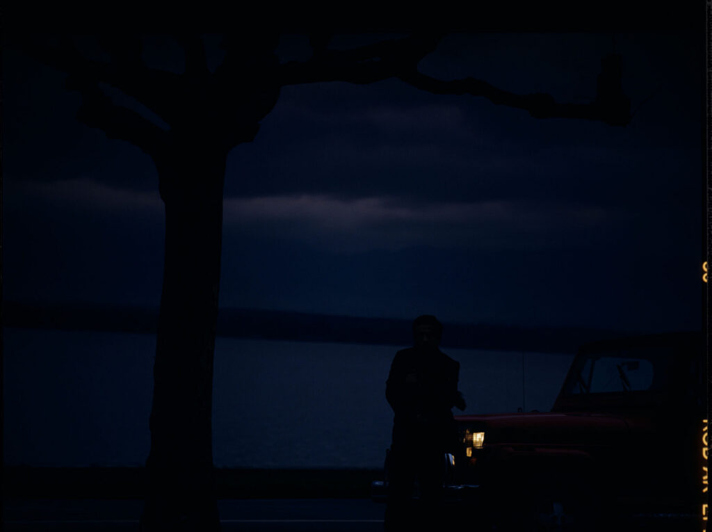 Auguste (Jean-Pierre Lorit) by the car.