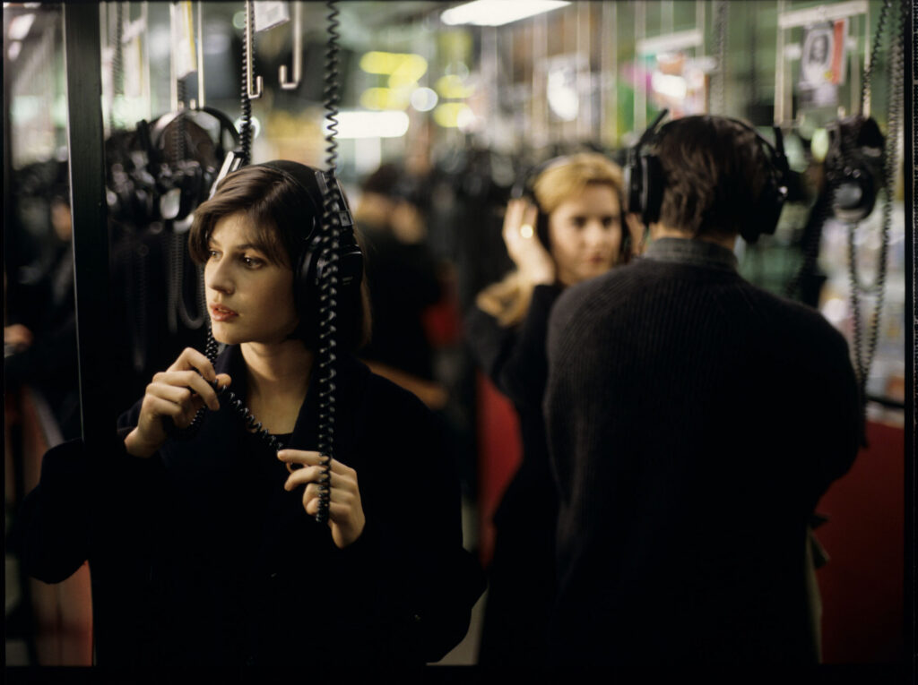 Valentine (Irène Jacob) listens to a record by Dutch composer Van den Budenmayer (Zbigniew Preisner) in a music store.