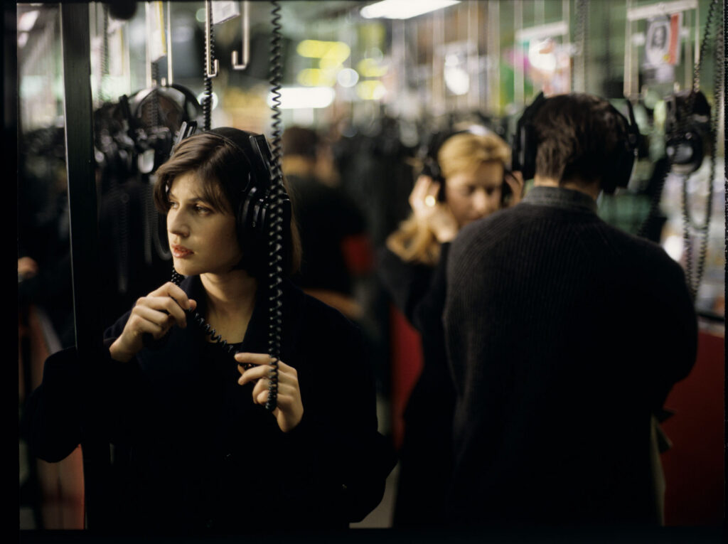 Valentine (Irène Jacob) listens to a record by Dutch composer Van den Budenmayer (Zbigniew Preisner) in a music store.