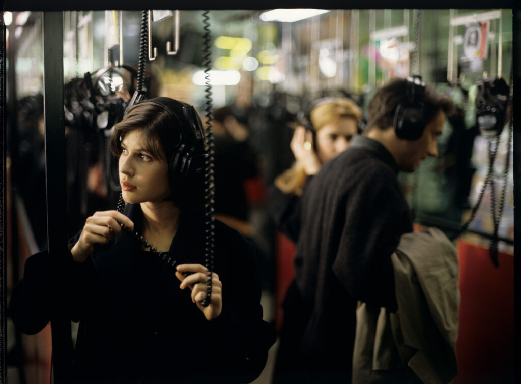 Valentine (Irène Jacob) listens to a record by Dutch composer Van den Budenmayer (Zbigniew Preisner) in a music store.