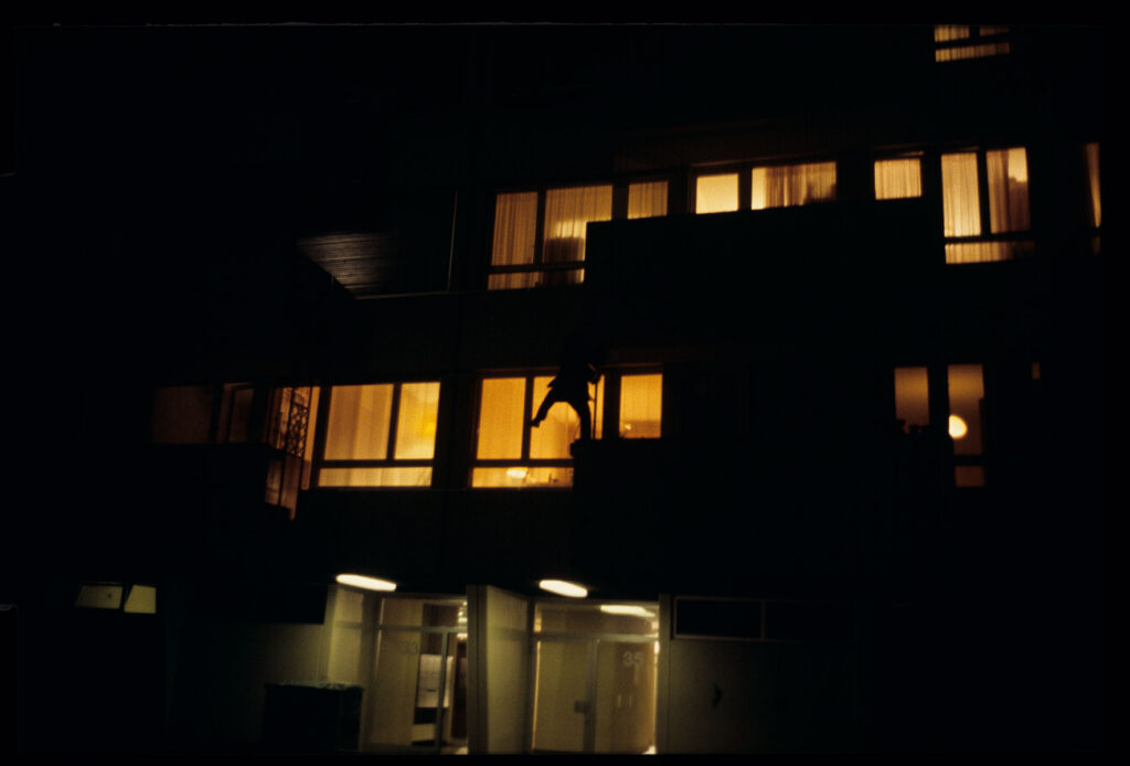 Auguste (Jean-Pierre Lorit) climbs the facade of a building to look through the window into his girlfriend's apartment.