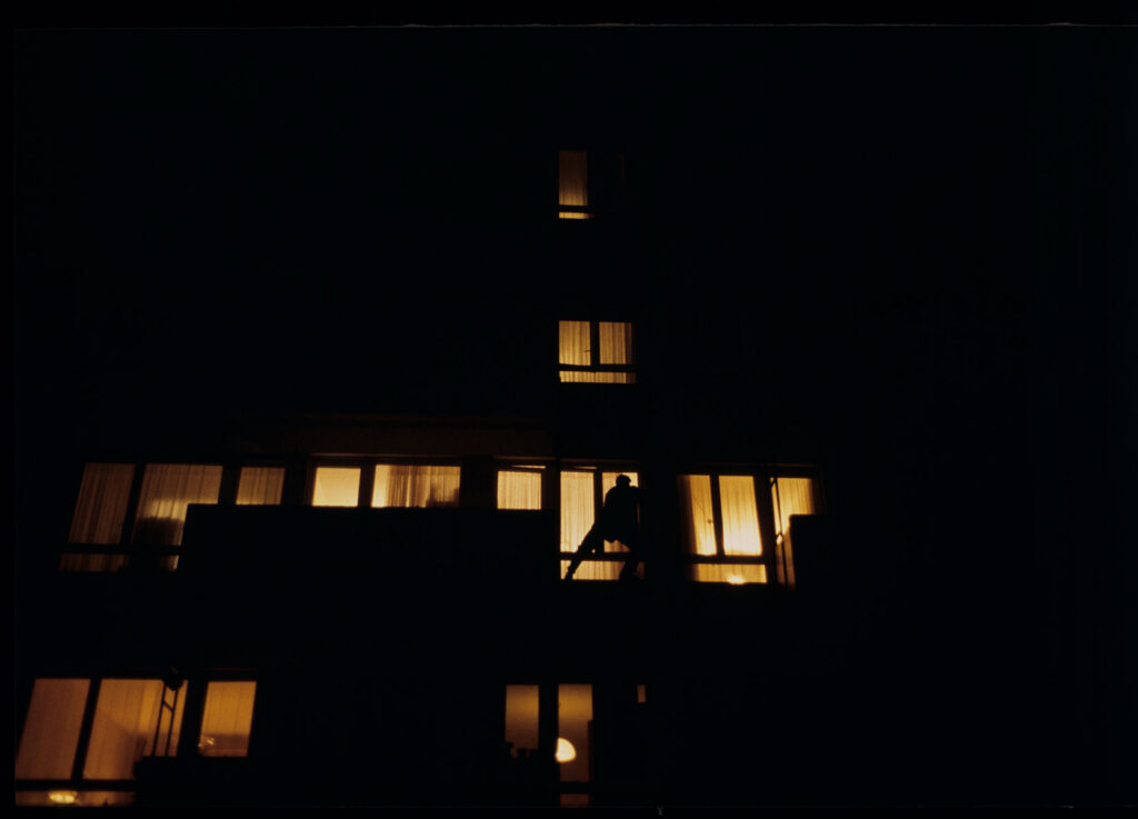 Auguste (Jean-Pierre Lorit) climbs the facade of a building to look through the window into his girlfriend's apartment.