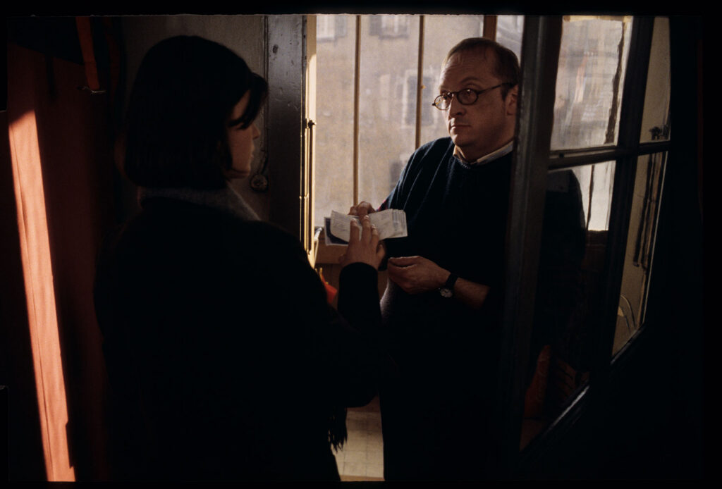 A neighbor (Jean Schlegel) brings Valentine (Irène Jacob) money that the postman left for her.