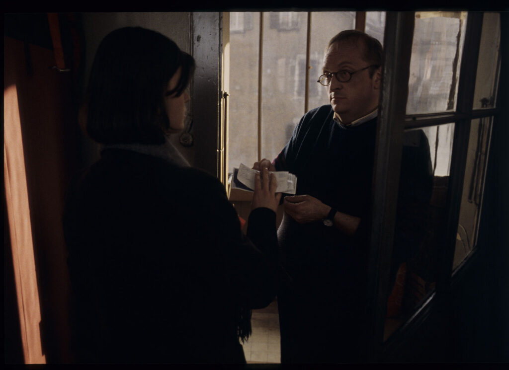 A neighbor (Jean Schlegel) brings Valentine (Irène Jacob) money that the postman left for her.