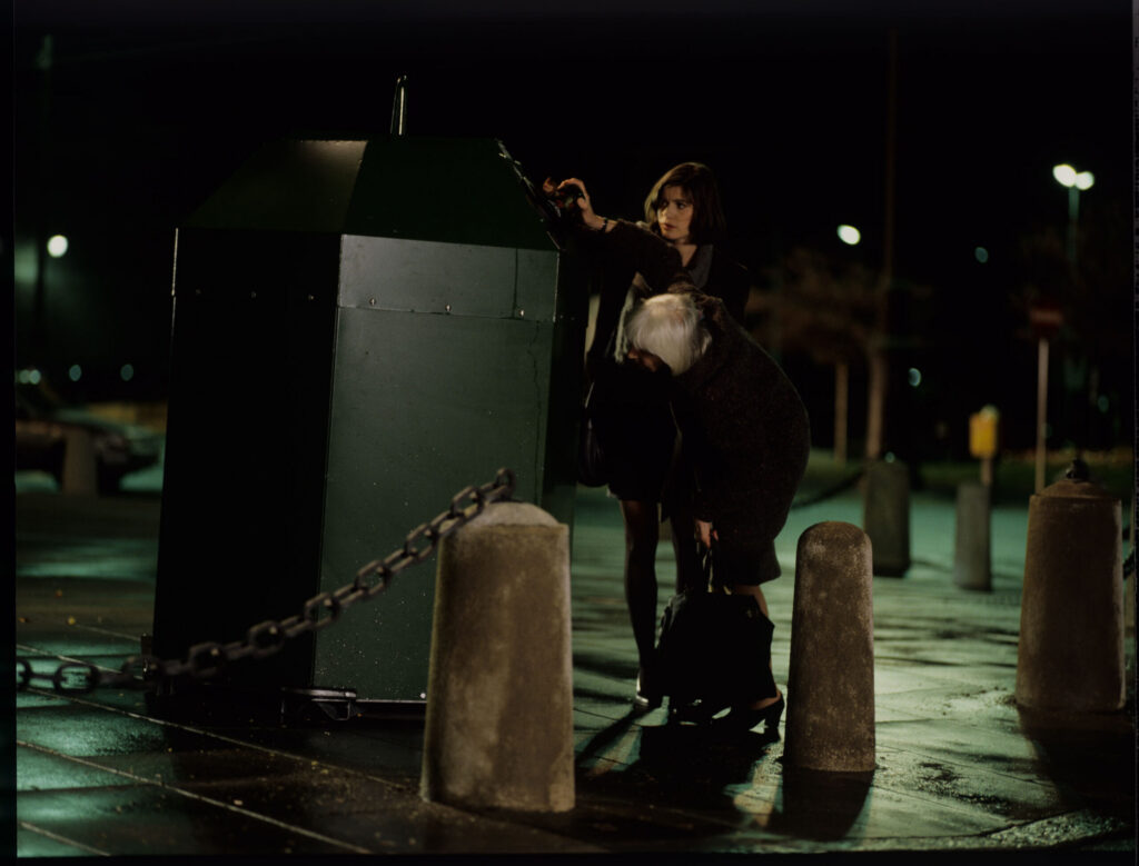 Valentina (Irène Jacob) helps an elderly woman throw a bottle into the recycling bin.