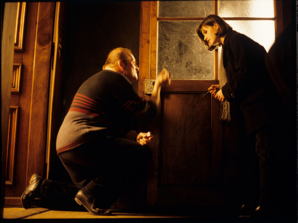 Valentine (Jacob) can't get into her apartment because the lock is stuck with chewing gum. A neighbor (Schlegel) helps her.