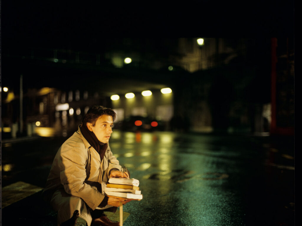 Auguste (Jean-Pierre Lorit) collecting books that he has dropped on the street.