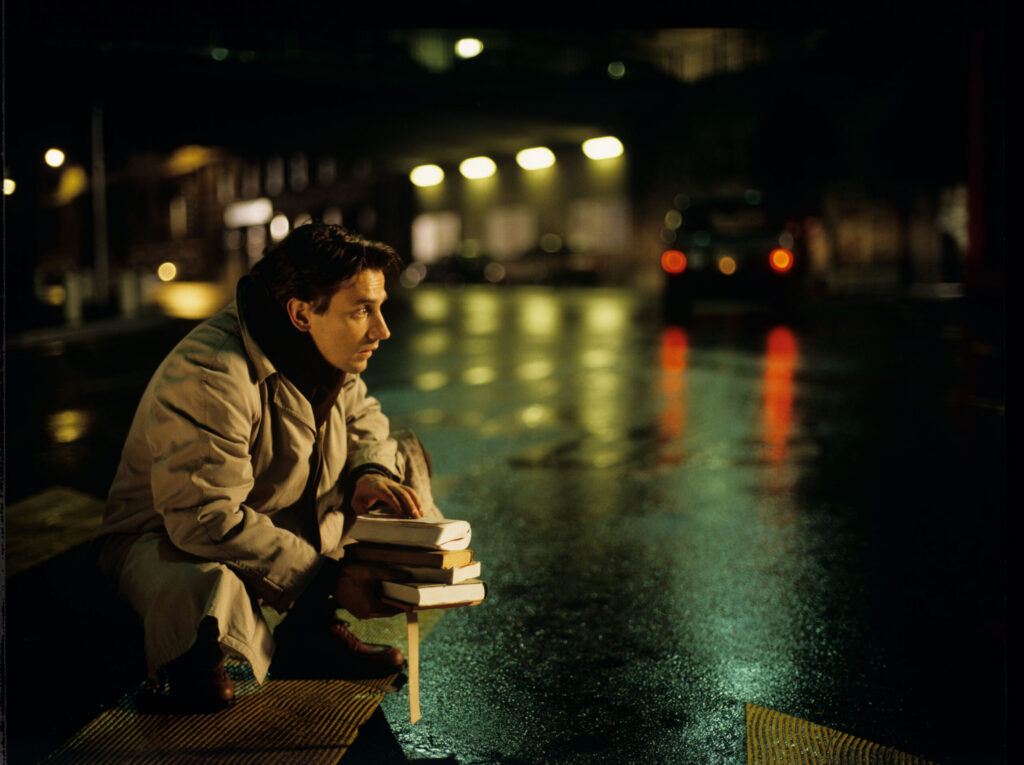 Auguste (Jean-Pierre Lorit) collecting books that he has dropped on the street.