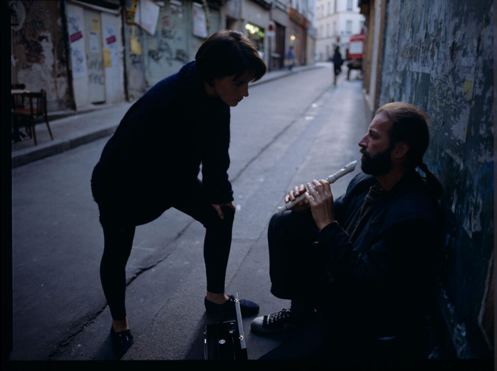 Julie (Juliette Binoche) talks to a street flautist (played by Jacek Ostaszewski - Polish composer and jazz musician).
