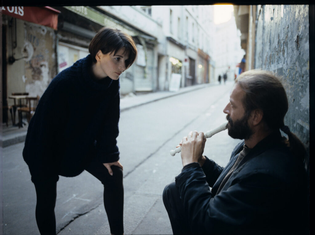 Julie (Juliette Binoche) talks to a street flautist (played by Jacek Ostaszewski - Polish composer and jazz musician).