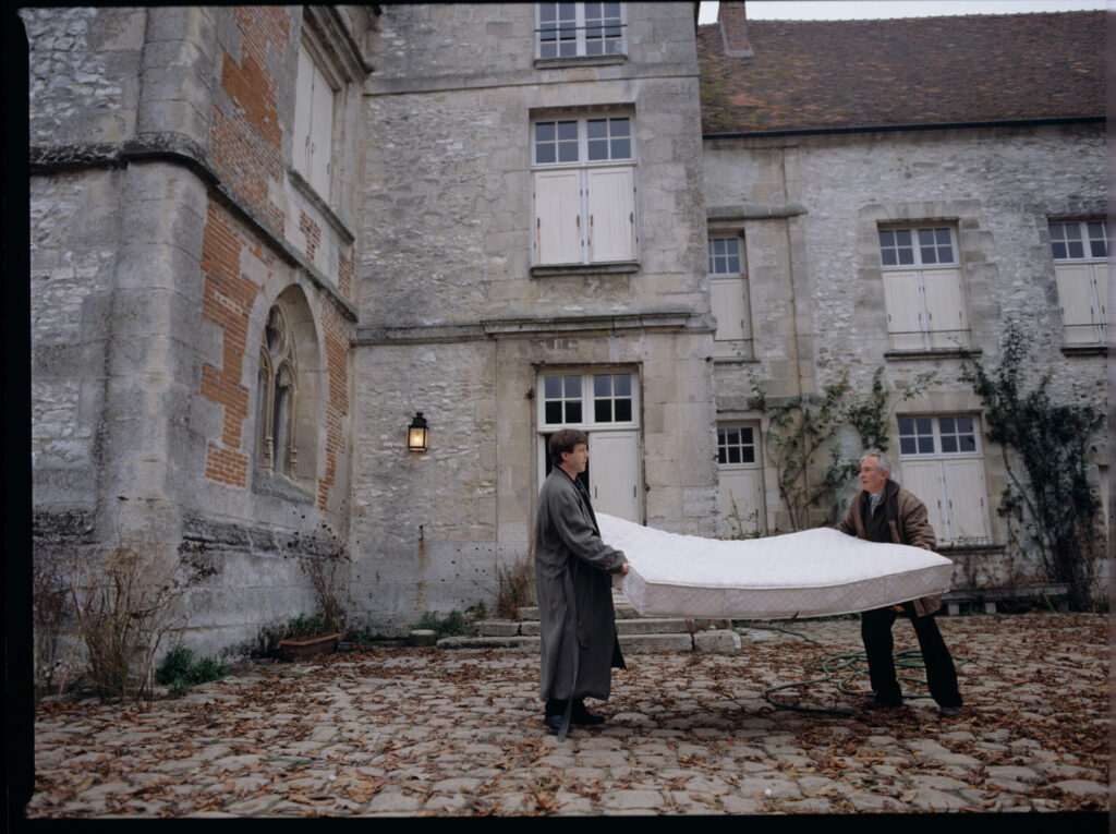 Oliviere (Régent) carries the mattress to the car with the help of a gardener (Forget). The scene was not shown in the film.
