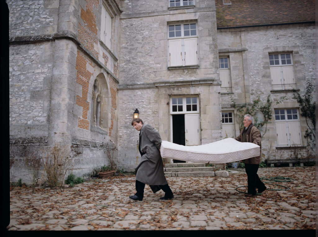 Oliviere (Régent) carries the mattress to the car with the help of a gardener (Forget). The scene was not shown in the film.