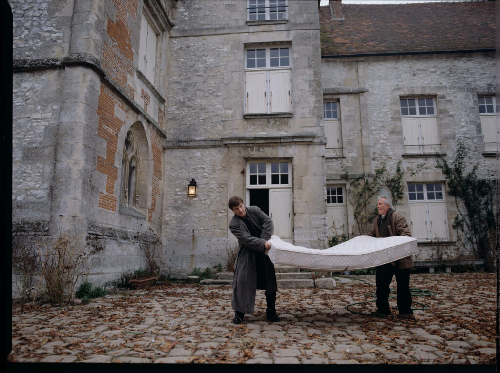 Oliviere (Régent) carries the mattress to the car with the help of a gardener (Forget). The scene was not shown in the film.